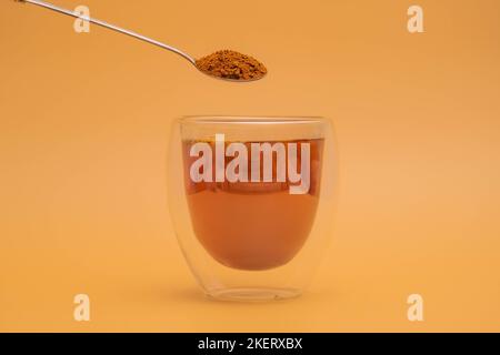 Weibliche Hand gießt Instant-Kaffee in doppelschichtige klare Glas mit gekochtem Wasser mit Löffel auf vintage Farbe Hintergrund. Stockfoto