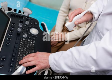 Teilansicht des Arztes mit der Konsole eines Ultraschallgeräts in der Nähe einer Frau in der Klinik, Stockbild Stockfoto