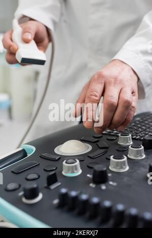 Teilansicht eines unscharfen Arztes, der die Sonde während der Verwendung eines Ultraschallgeräts hält, Stockbild Stockfoto