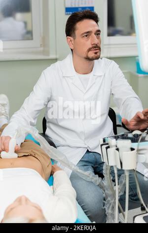 Aufmerksamer Arzt im weißen Mantel, der Nieren Ultraschall des Patienten in der Klinik macht, Stockbild Stockfoto