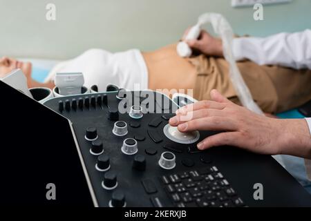 Teilansicht des Arztes, der das Ultraschallgerät betreibt, während er die abdominale Untersuchung einer verschwommenen Frau macht, Stockbild Stockfoto