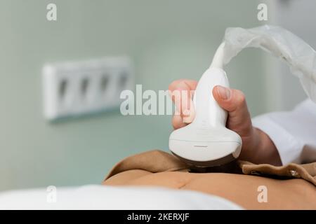 Ultraschallsonde in der Hand des Arztes, der die Abdominaluntersuchung der Frau in der Klinik macht, Stockbild Stockfoto