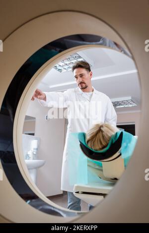 Arzt im weißen Mantel Betrieb Computertomographie Maschine während der Untersuchung der Frau, Stock Bild Stockfoto