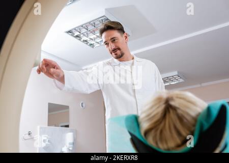 Brünett Radiologe in weißer Schicht Betrieb Computertomographie Scanner in der Nähe des Patienten, Stock Bild Stockfoto