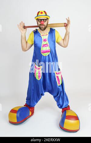 Urlaubskonzept. Der Clown ist ein Mann in einem leuchtend blauen und gelben Anzug mit einem Baseballschläger. Stockfoto