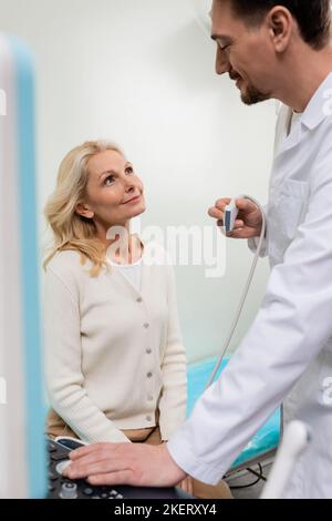 Glücklicher Arzt mit Ultraschall-Sonde Blick auf glückliche blonde Frau im Krankenhaus, Stockbild Stockfoto