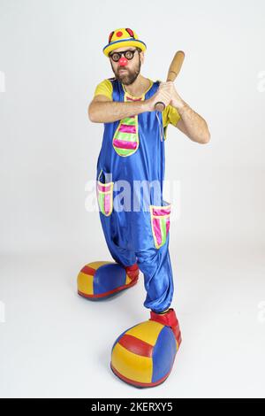Urlaubskonzept. Der Clown ist ein Mann in einem leuchtend blauen und gelben Anzug mit einem Baseballschläger. Stockfoto