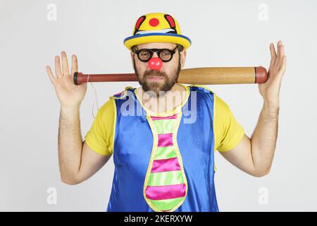 Urlaubskonzept. Der Clown ist ein Mann in einem leuchtend blauen und gelben Anzug mit einem Baseballschläger. Stockfoto