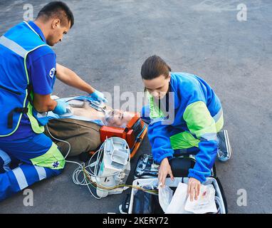 Sanitäter, die die HLW mit einem mobilen Defibrillator durchführen, wenn der Patient auf einer Liege im Freien liegt. Rettungskräfte, HLW Stockfoto