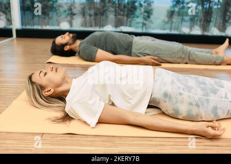 Shavasana. Mann mit Frau in Sportkleidung praktiziert Yoga, während sie sich in Savasana oder Leichenhaltung im Wellness-Center hinlegt Stockfoto