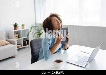 Betont afroamerikanischen Freiberufler hält Notebook in der Nähe von Geräten und Tee zu Hause, Bild Stock Stockfoto