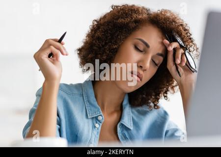 Müde afroamerikanische Frau mit geschlossenen Augen halten Brille und Stift, Stock Bild Stockfoto