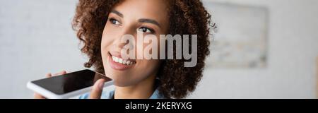 Fröhliche afroamerikanische Frau mit lockigen Haaren, die Sprachnachricht auf Smartphone, Banner, Stockbild aufzeichnet Stockfoto