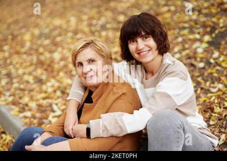 Porträt der alten Rentnerin Mutter und mittleren Alters fröhliche Tochter verbringen Zeit zusammen im Freien in der fallenden Saison. Kaukasische ältere Mutter und ihre Tochter sitzen in entzückenden Herbstpark Stockfoto