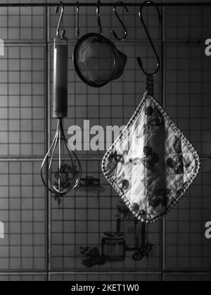Alte italienische Vintage Küchenutensilien. Topflader, Sieb und Schneebesen hängen an Regalen an der Küchenwand. Stockfoto