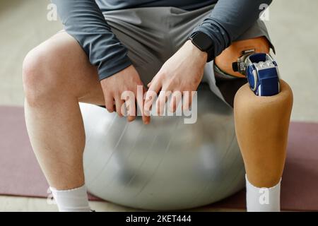 Nahaufnahme eines Mannes mit Beinprothese, der während des Heimtrainings auf dem Fitnessball sitzt Stockfoto