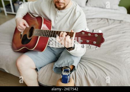 Nahaufnahme eines Mannes mit Beinprothese, der zuhause Gitarre spielt, Platz kopieren Stockfoto