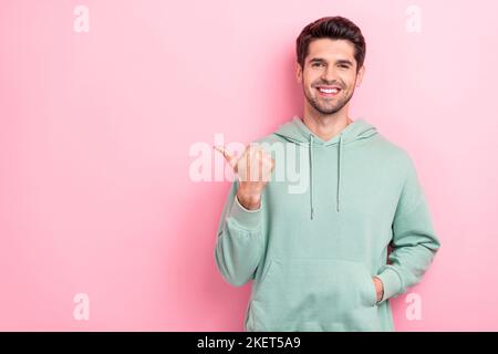 Portrait Foto von positiven fröhlichen Kerl tragen khaki trendy Pullover legte Hand Tasche Regie Finger leeren Raum Tipps auf rosa Hintergrund isoliert Stockfoto