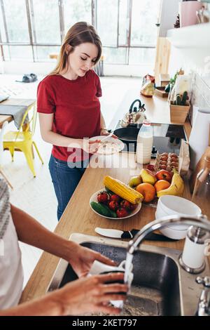 Zwei Freundinnen in der Küche bereiten Frühstück Kochen und Geschirr waschen. Stockfoto