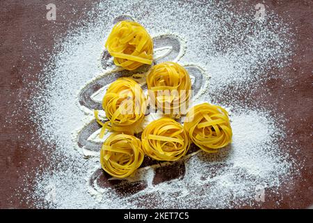 Rohe gelbe italienische Pasta (Nester) Pappardelle, Fettuccine oder Tagliatelle in Form eines Weihnachtsbaums auf braunem Hintergrund, Nahaufnahme. Ei hausgemacht Stockfoto