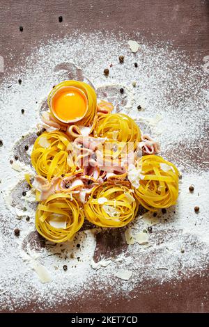 Rohe gelbe italienische Pasta (Nester) Pappardelle, Fettuccine oder Tagliatelle in Form eines Weihnachtsbaums auf braunem Hintergrund, Nahaufnahme. Ei hausgemacht Stockfoto