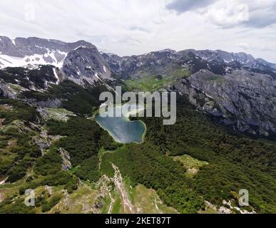 Luftaufnahme des herzförmigen Sees im Trnovacko See in Montenegro. See umgeben von Bergen mit Schnee. Wanderleben. Reisen und Abenteuer Stockfoto