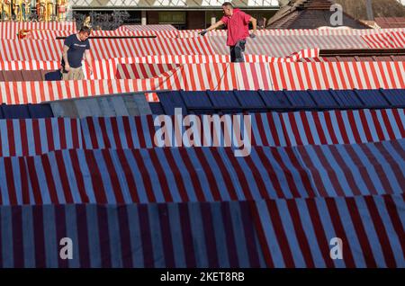 Nürnberg, Deutschland. 14.. November 2022. Zwei Männer stellen die rot-weiß gestreifte Dachplane während der Aufstellarbeiten am Nürnberger Christkindlesmarkt auf einen Stand. Der Nürnberger Christkindlesmarkt wird am 25. November eröffnet. Quelle: Daniel Karmann/dpa/Alamy Live News Stockfoto