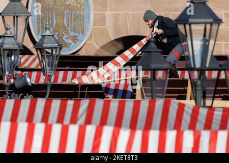 Nürnberg, Deutschland. 14.. November 2022. Ein Standbetreiber platziert die rot-weiß gestreifte Dachplane während der Aufstellarbeiten am Nürnberger Christkindlesmarkt auf seinem Stand. Der Nürnberger Christkindlesmarkt wird am 25. November eröffnet. Quelle: Daniel Karmann/dpa/Alamy Live News Stockfoto