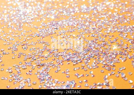 Konfetti aus glänzendem Silberkristall auf gelbem Hintergrund. Selektiver Fokus. Leuchtende Textur. Stockfoto
