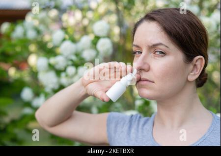 Kaukasische Frau verwendet ein Nasenspray, während sie im Park spazieren geht. Stockfoto