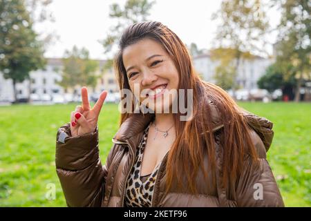Porträt einer lächelnden Chinesin, die mit ihrer Hand das Siegeszeichen macht Stockfoto