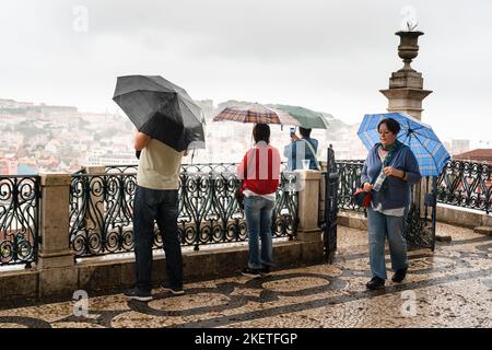 Touristen nehmen Deckung, während in den verdeckten Teilen der Stadt im Miradouro de São Pedro de Alcântara in Lissabon, Portugal, starker Regen herrscht. Stockfoto