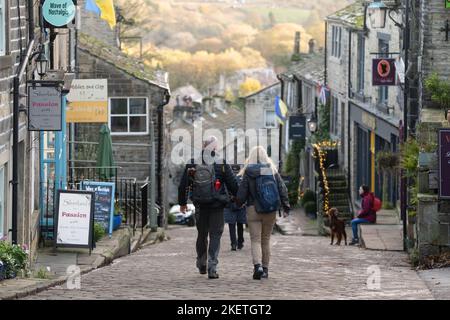 Haworth, West Yorkshire, Großbritannien. Ein Paar, das im Herbst die gepflasterte Hauptstraße entlang läuft. Stockfoto