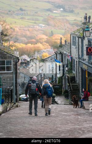 Haworth, West Yorkshire, Großbritannien. Ein Paar, das im Herbst die gepflasterte Hauptstraße entlang läuft. Stockfoto