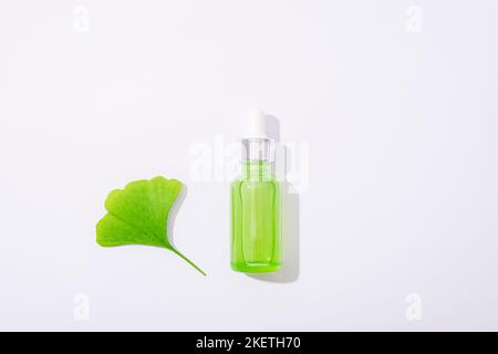 Grüne Serumflasche und Ginkgo-Biloba-Blatt auf weißem Hintergrund. Konzept der Naturkosmetik. Draufsicht, flach liegend. Stockfoto