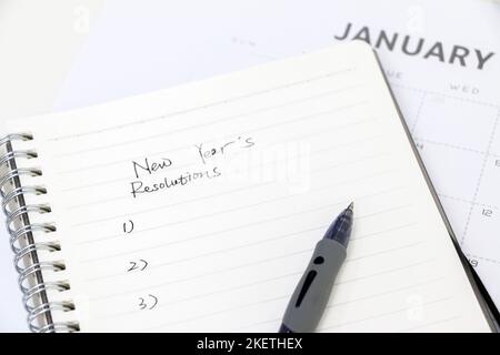 Neujahrsvorsätze schreiben, Notizblock mit Kugelschreiber aufschreiben, Januar-Kalender im Hintergrund, selektiver Fokus. Ziele für das neue Jahr setzen. Stockfoto