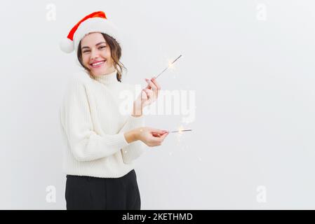 Schöne junge Frau in weißem Pullover hält Wunderkerzen und lacht, lächelt mit einem breiten Lächeln Stockfoto