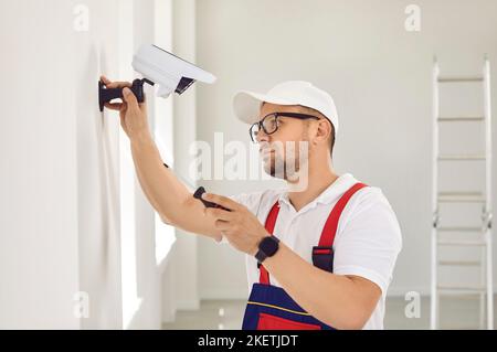 Ein kaukasischer Mann in Uniform und Brille hält einen Schraubendreher und installiert Videoüberwachung. Stockfoto