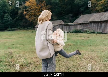 Mama umkreist ihre kleine Tochter während eines Spaziergangs auf dem Bauernhof. Stockfoto