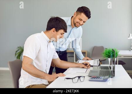 Zwei glückliche junge Männer, die im Büro arbeiten und sich einige Geschäftsdokumente anguckt Stockfoto