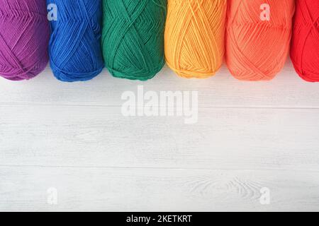 Viele bunte Fadenbälle auf gestricktem Stoff auf weißem Holzhintergrund. Garn aus hellen bunten Blumen, Stricken und Häkeln. Nadelwor Stockfoto