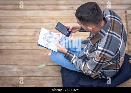 Ein junger Mann mit einer Papierkarte und einem Smartphone in der Hand, Draufsicht. Stockfoto