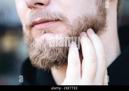 In Nahaufnahme berührt ein junger Mann seinen Bart mit der Hand. Stockfoto