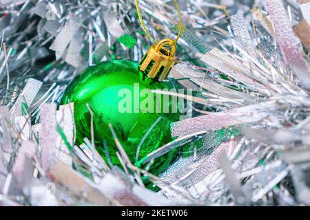 Ein grüner Weihnachtsball liegt zwischen dem Neujahrsfest, flauschig-silbernem Lametta Stockfoto