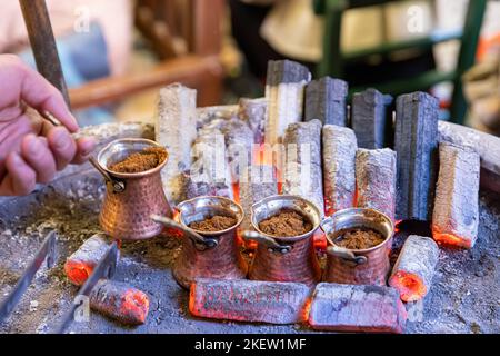 Türkischer Kaffee auf Glut gekocht. Straßenverkäufer kocht türkischen Kaffee auf Glut. Es werden traditionelle Töpferwaren und türkische Kaffeetassen verwendet. Gedreht in einem Café in Stockfoto