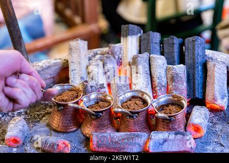 Türkischer Kaffee auf Glut gekocht. Straßenverkäufer kocht türkischen Kaffee auf Glut. Es werden traditionelle Töpferwaren und türkische Kaffeetassen verwendet. Gedreht in einem Café in Stockfoto