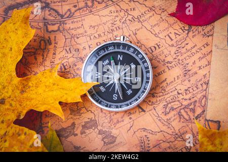 Reisekompass auf der Karte in hellen bunten Herbstblättern. Navigation im Herbst.. Stockfoto