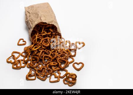 Herzförmige, salzige Brezel-Snacks, die aus dem Papierbeutel auf Weiß verschüttet wurden Stockfoto