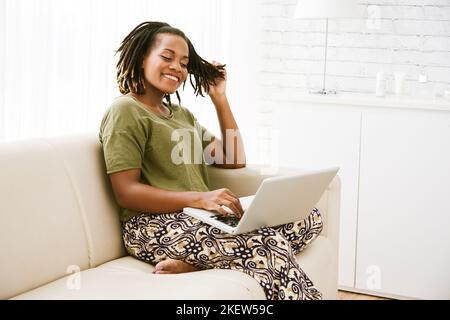 Eine ziemlich fröhliche Frau, die mit einem Laptop Nachrichten liest und mit Freunden kommuniziert Stockfoto