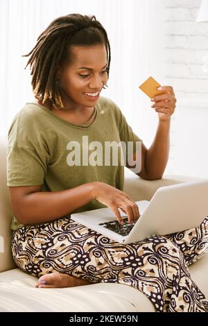 Ziemlich lächelnde Frau, die auf dem Sofa sitzt und online einkaufen geht Stockfoto